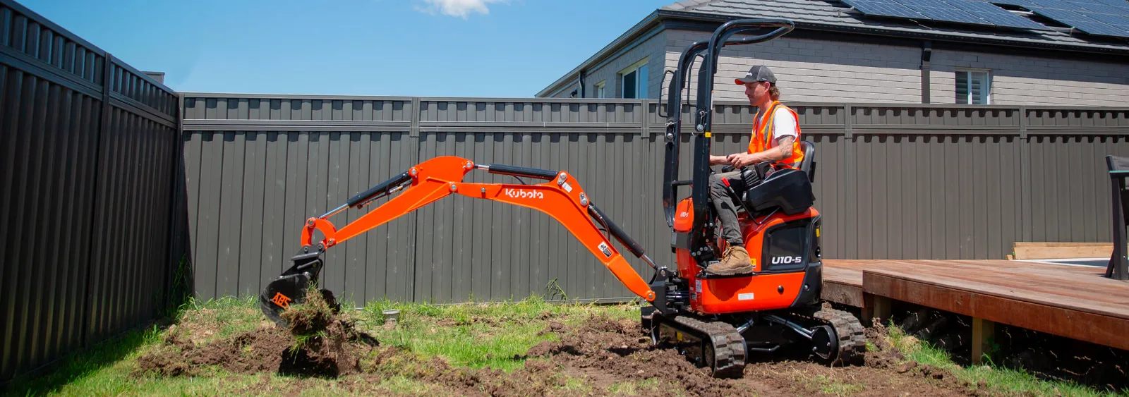 Kubota U10-5 1.2 tonne excavator digging in a suburban backyard beside a timber deck