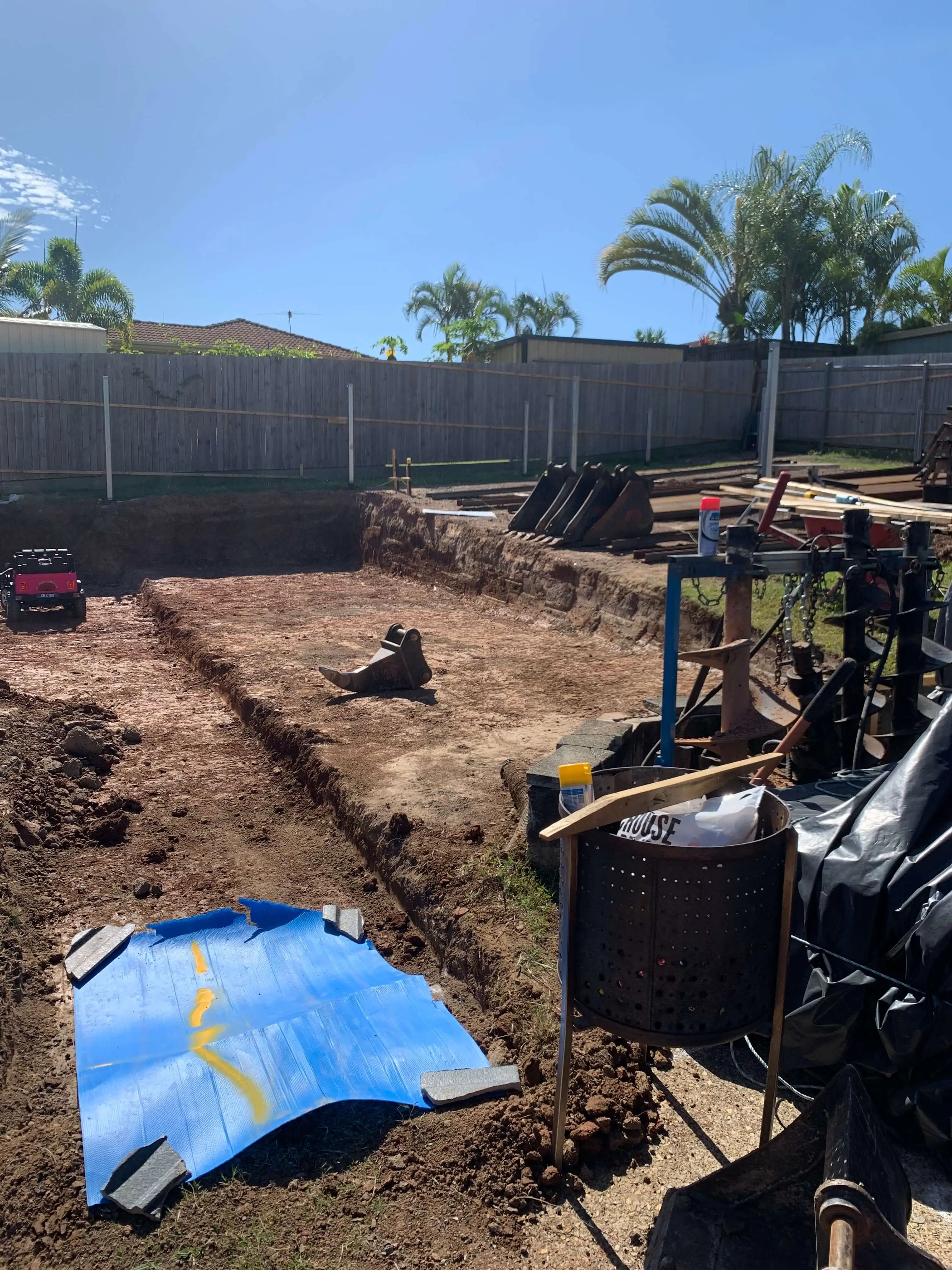 Excavated pad with excavator buckets and auger attachments laid out on site