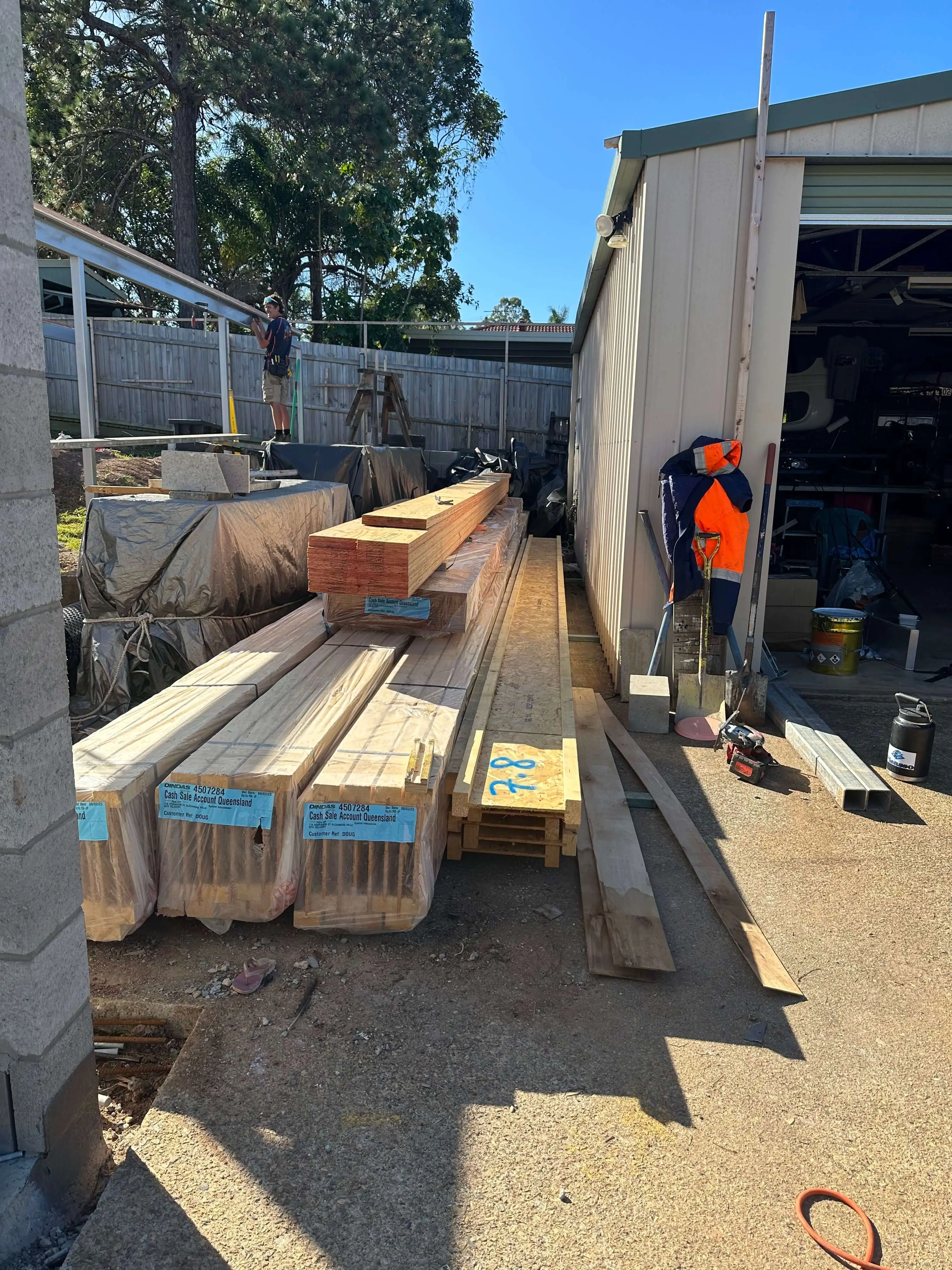 LVL beams and framing timber stacked on site beside a shed, ready for installation