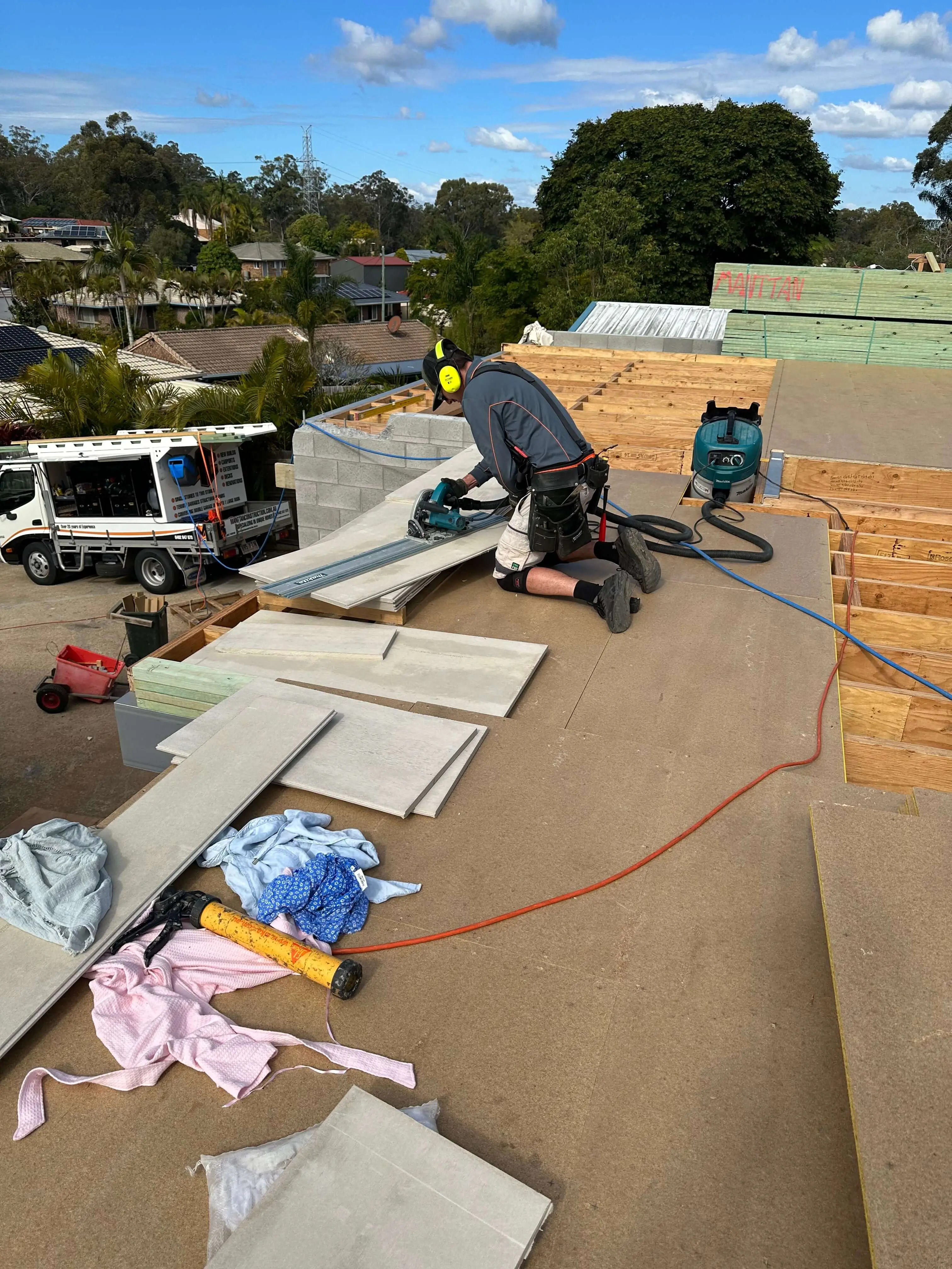 Carpenter cutting sheet flooring on an upper-floor frame above a Manttan Construction truck